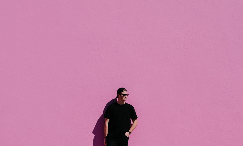 Man-iklädd-svarta-kläder-står-mot-rosa-vägg
