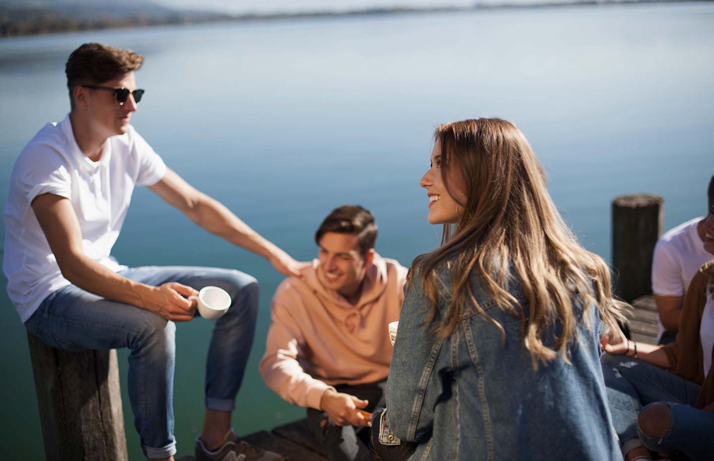 Grupp vänner dricker kaffe vid sjö.